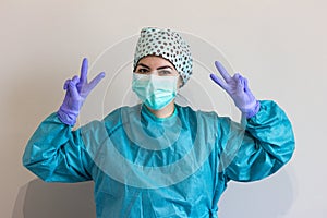 A nurse in a medical uniform with hygienic face surgical medical mask and gown, making a peace sign