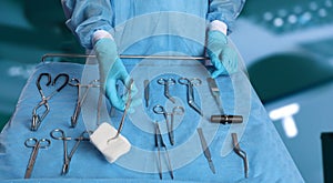 Nurse near table with different surgical instruments in operating room, closeup