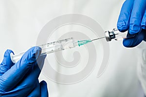 Nurse of NHS medical lab technician inserting syringe needle into glass vial bottle photo