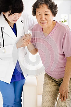 Nurse in nursing home helping senior woman stand up