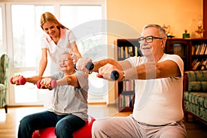 Nurse at nursing home helps senior people to doing exercises