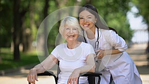 Nurse and old handicapped woman smiling at camera and showing thumbs-up gesture