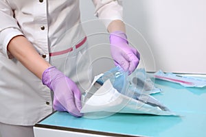 A nurse opens a craft bag with sterile dental instruments. Photo without a face. Gloved hand. Copy of the space. Gray background