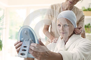 Nurse and patient with cancer wearing headscarf and looking at the mirror.