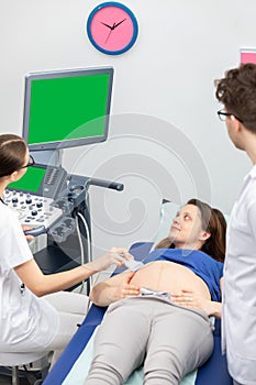 A nurse performs an ultrasound on a pregnant patient under the guidance of the attending doctor.