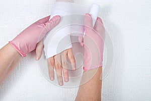 Nurse with pink gloves wrapping young girls hand with gauze dressing