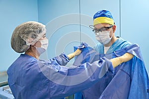 Nurse in preoperative room helps surgeon put on sterile gown