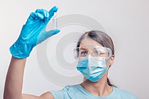 Nurse in protective gloves and mask holding glass vial with injection liquid. Vaccination against influenza and coronavirus