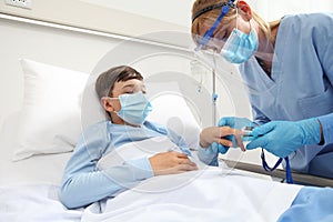 Nurse with pulse oximeter on patient child in hospital bed, wearing protective visor mask, corona virus covid 19 protection