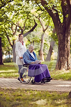 Nurse pushing elderly man in wheelchair while reading book