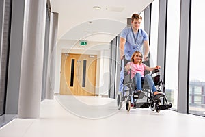 Nurse Pushing Girl In Wheelchair Along Corridor