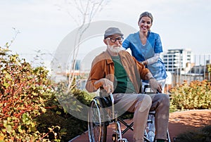 Nurse pushing senior man in wheelchair. Female caregiver and elderly man enjoying a warm autumn day in nursing home.