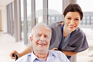 Nurse Pushing Senior Patient In Wheelchair Along Corridor