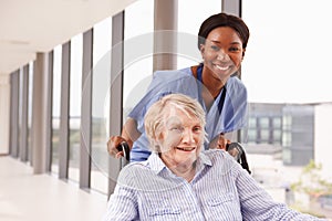 Nurse Pushing Senior Patient In Wheelchair Along Corridor