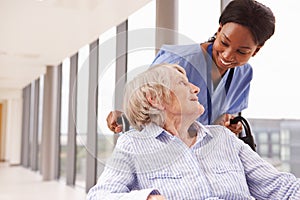 Nurse Pushing Senior Patient In Wheelchair Along Corridor photo