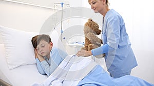 Nurse puts child to sleep with his teddy bear in the hospital bed