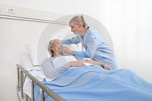 Nurse puts oxygen mask on elderly woman patient lying in the hospital room bed, coronavirus covid 19 protection concept.