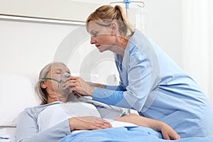 Nurse puts oxygen mask on elderly woman patient lying in the hospital room bed