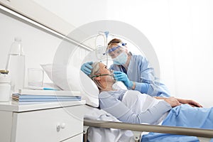 Nurse puts oxygen mask on elderly woman patient lying in the hospital room bed, wearing protective gloves and visor medical mask,