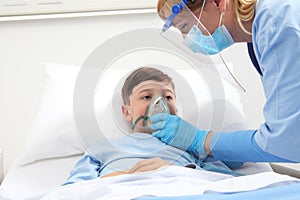 nurse puts oxygen mask on patient child in hospital bed, wearing protective visor mask, corona virus covid 19 protection concept, 