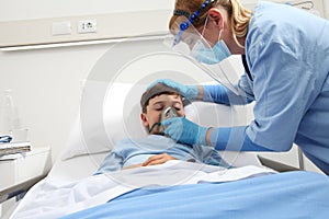 nurse puts oxygen mask on patient child in hospital bed, wearing protective visor mask, corona virus covid 19 protection concept, 