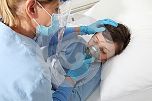 nurse puts oxygen mask on patient child in hospital bed, wearing protective visor mask, corona virus covid 19 protection concept, 