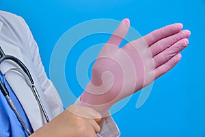 A nurse puts a protective medical glove on her arm, close-up on a blue background
