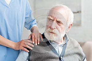 Nurse putting hands on shoulder of sad grey man