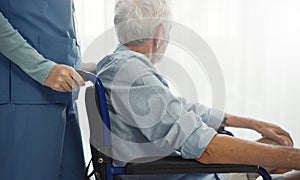 Nurse putting wheelchair with senior man  window. Unhappy senior man having geriatric or depression disease. Therapist taking care