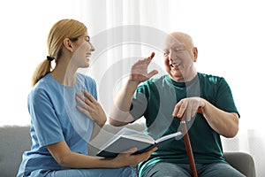 Nurse reading book to elderly man. Assisting senior people