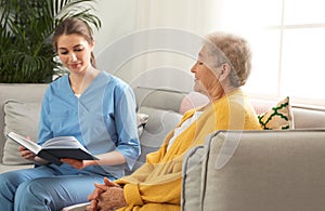 Nurse reading book to elderly woman indoors