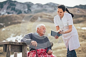 Nurse reading book to gray hair senior man outdoor