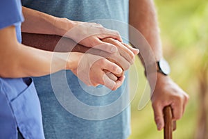 A nurse and senior patient holding hands while helping him to walk outside. Closeup of an elderly man being supported by