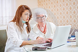 Nurse and senior woman looking together at medical record on laptop.