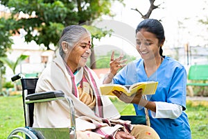 Nurse and senior woman on wheel chair laughing by reading book or novel at park - concept of relaxation, professional