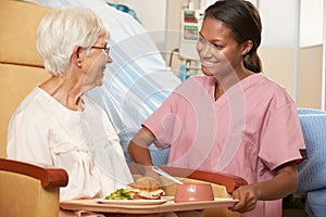 Nurse Serving Meal To Senior Female Patient Sitting In Chair