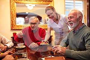 Nurse serving tea while older people play board games, retirement home