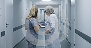 Nurse shows MRI scan image to female doctor in clinic corridor using tablet