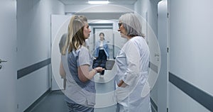 Nurse shows MRI scan image to female doctor in clinic corridor using tablet