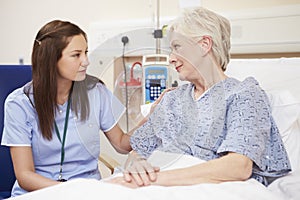 Nurse Sitting By Female Patient's Bed In Hospital