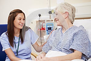 Nurse Sitting By Female Patient's Bed In Hospital