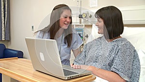 Nurse Sitting By Female Patient's Bed In Hospital