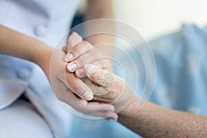 Nurse sitting on a hospital bed next to an older woman helping hands, care for the elderly concept