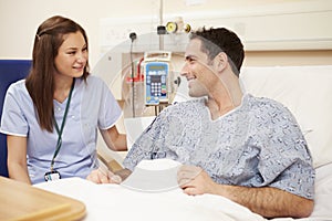 Nurse Sitting By Male Patient's Bed In Hospital