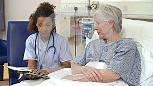 Nurse Sitting By Senior Female Patient's Bed In Hospital