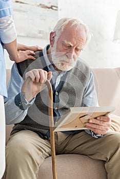 Nurse standing near upset grey haired man with photo frame