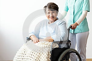 Nurse supporting happy disabled senior woman in a wheelchair