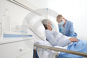 Nurse with the syringe injects the vaccine to the elderly woman patient lying in the hospital room bed, wearing protective gloves