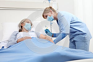 Nurse with the syringe injects the vaccine to the elderly woman patient lying in the hospital room bed, wearing protective gloves