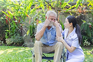 Nurse take care a depressed thoughtful senior retirement man on his wheelchair in a garden in his home